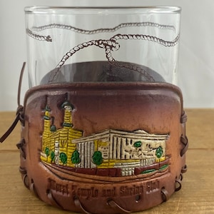 May include: A brown leather wrapped glass tumbler with a rope design around the top. The leather has a picture of the Salt Lake Temple and Shrine in Salt Lake City, Utah.
