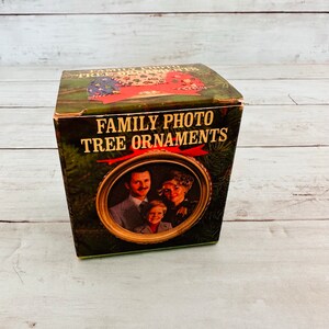 May include: A green box with the text "FAMILY PHOTO TREE ORNAMENTS" on the front. The box has a picture of a family of three on the front, with a gold frame.