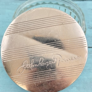 May include: Silver lid with a ribbed design and the inscription "John Robert Powers" in cursive.