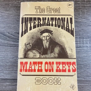 May include: A vintage book titled "The Great International Math On Keys Book" with a brown cover and a black and white illustration of a man with a beard and a calculator. The book has a red and white price tag that says "495".