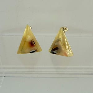 May include: A pair of triangular earrings with a gold-colored post. The earrings are a translucent yellow with internal inclusions of red, black, and white. The earrings are set against a white background.