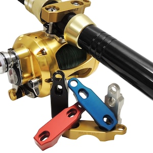 Pode incluir: Um close-up de um carretel de pesca dourado com uma vara preta anexada. O carretel tem uma linha verde e a vara tem uma alça preta. Existem quatro peças de metal de cores diferentes, vermelho, azul, preto e prata, que são usadas para conectar a vara ao carretel.