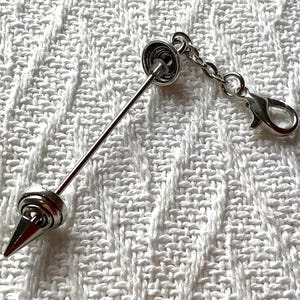 May include: A silver-toned metal collar bar featuring a pointed spike end and a circular base. The accessory includes a short chain attached to a lobster claw clasp, allowing it to be secured to clothing or other items with a polished finish.