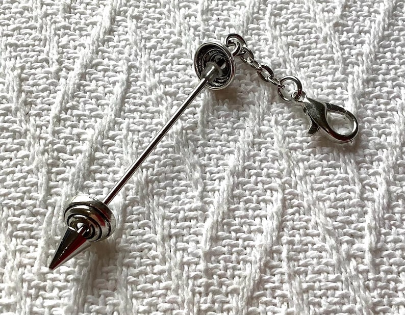 May include: A silver-toned metal collar bar featuring a pointed spike end and a circular base. The accessory includes a short chain attached to a lobster claw clasp, allowing it to be secured to clothing or other items with a polished finish.