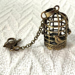 May include: A gold-toned birdcage pendant with a small bird perched inside. The cage is attached to a chain with a bird-shaped clasp.