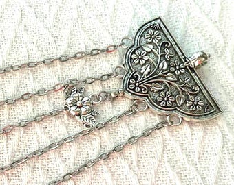 May include: Silver-toned, multi-strand body jewelry. The piece features a triangular, floral-patterned centerpiece and delicate chain links. Additional floral accents are incorporated along the chains, creating an elegant, bohemian aesthetic.