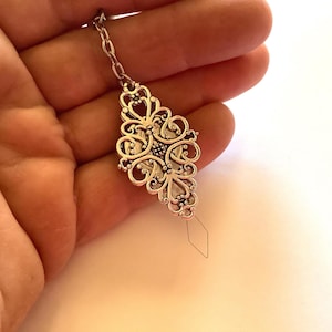 May include: Silver threader with a decorative filigree design. The threader has a small diamond-shaped opening at the end.