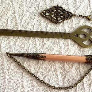 Pode incluir: Uma variedade de acess&oacute;rios antigos em tom de lat&atilde;o, incluindo uma r&eacute;gua em forma de chave, um pingente decorativo e um l&aacute;pis com extremidades met&aacute;licas decorativas. A r&eacute;gua em forma de chave mede aproximadamente 25 cm de comprimento. Todos os itens t&ecirc;m uma est&eacute;tica vintage.