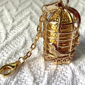 May include: A gold-tone birdcage charm with a small bird inside. The cage is attached to a gold-tone chain with a lobster clasp.