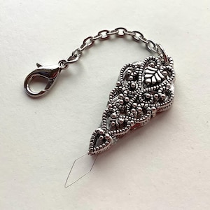 May include: Silver filigree charm with a chain and a lobster clasp. The charm is shaped like a teardrop with a pointed tip.