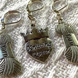 May include: Silver-toned yarn-themed earrings. Two earrings feature a yarn ball charm with the word "Yarn" on a rectangular tag. The third earring has a heart-shaped charm with a crown and the words "Knitting Queen".