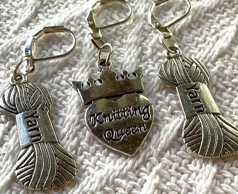 May include: Silver-toned yarn-themed earrings. Two earrings feature a yarn ball charm with the word "Yarn" on a rectangular tag. The third earring has a heart-shaped charm with a crown and the words "Knitting Queen".