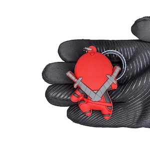 Peut inclure: Un porte-cl&eacute;s en forme de personnage de dessin anim&eacute; rouge et gris avec un anneau. Le personnage tient deux &eacute;p&eacute;es et porte un casque rouge.