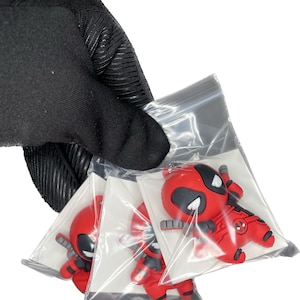 Peut inclure: Trois porte-cl&eacute;s en caoutchouc repr&eacute;sentant le personnage de Deadpool, en rouge et noir, dans des sachets en plastique transparent individuels. Les porte-cl&eacute;s sont en caoutchouc et ont un design 3D.