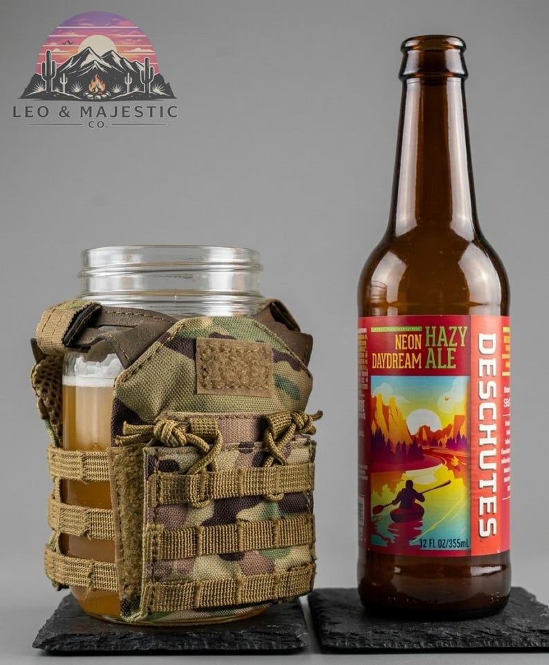 Puede incluir: Un tarro de cristal transparente con una funda de camuflaje que contiene un vaso de cerveza, junto a una botella de cerveza marr&oacute;n con una etiqueta roja y amarilla que dice "NEON HAZY DAYDREAM ALE". La etiqueta tambi&eacute;n dice "DESCHUTES" y "355ml". El logo "LEO & MAJESTIC CO." es visible.