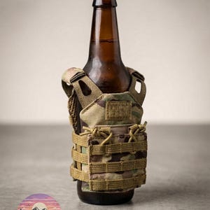 Puede incluir: Una botella de cerveza marr&oacute;n con tapa negra est&aacute; dentro de un enfriador tipo chaleco t&aacute;ctico con estampado de camuflaje. El enfriador tiene m&uacute;ltiples correas y un parche de velcro. El logotipo "LEO & MAJESTIC CO." est&aacute; en la parte inferior.