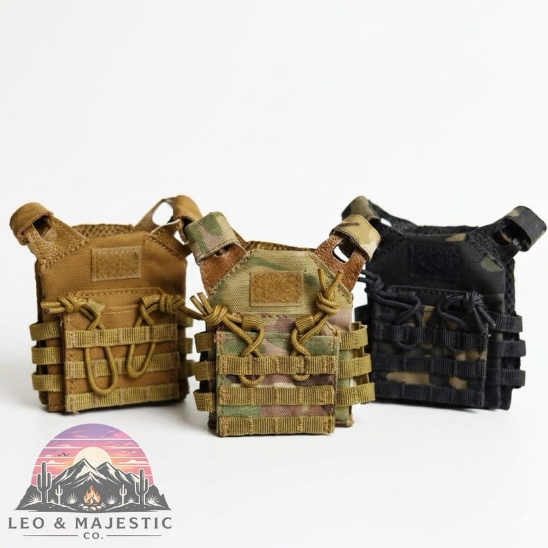 Puede incluir: Tres chalecos t&aacute;cticos en miniatura en color beige, camuflaje y negro. Cada chaleco cuenta con m&uacute;ltiples bolsillos, correas y un &aacute;rea de parche de velcro. Los chalecos se muestran sobre un fondo blanco.