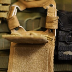 Puede incluir: Primer plano de un chaleco t&aacute;ctico en tonos beige, verde oliva y negro. El chaleco presenta m&uacute;ltiples correas, bolsillos y un parche de velcro. El dise&ntilde;o sugiere un enfoque en la funcionalidad y la durabilidad.