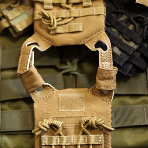 Puede incluir: Chaleco t&aacute;ctico color beige con m&uacute;ltiples correas y bolsillos. El chaleco presenta un dise&ntilde;o modular con una serie de correas para sujetar equipo adicional. La combinaci&oacute;n de colores es beige y verde oliva, con detalles en negro.