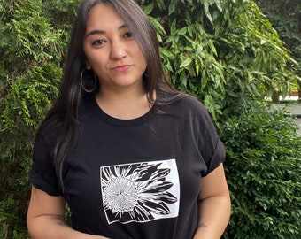 Könnte beinhalten: Schwarzes T-Shirt mit einem weißen Sonnenblumen-Motiv.