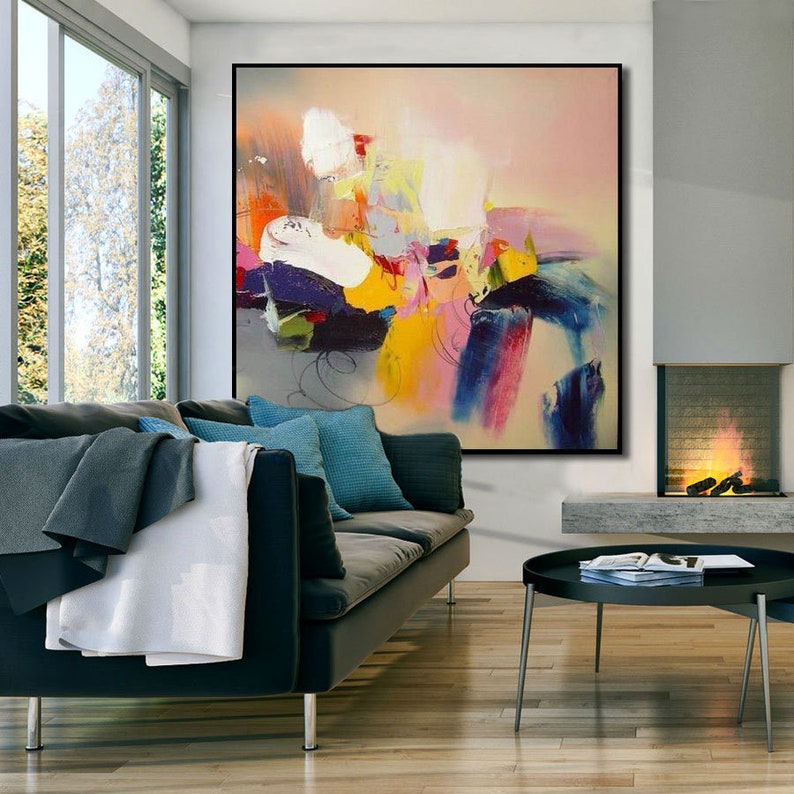 May include: Abstract painting with bold strokes of color in shades of pink, yellow, blue, green, and white. The painting is framed and hanging on a wall in a living room setting.