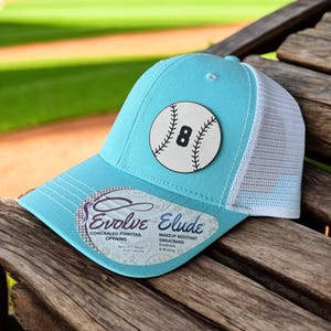 May include: A light blue baseball cap with a white mesh back. The cap has a white baseball with a black number 8 on it. The cap has the text "Evolve Concealed Ponytail Opening" and "Elude Makeup Resistant Sweatband Breathable & Wicking" on the side.