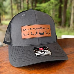 Charcoal Gray front and black mesh back Richardson 112 trucker hat with brown engraved leather rectangle patch reading '#AllRacksMatter' with deer antler and bra graphic; funny hunting gift hat for husband; snapback; adjustable.
