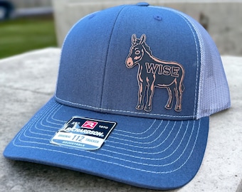 May include: A blue and gray trucker hat with a pink donkey graphic and the word "WISE" on the front. The hat is adjustable and has a Richardson 112 label.