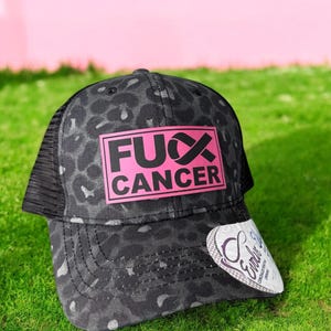 May include: Black and grey leopard print trucker hat with a pink square patch that says "FUX CANCER" in black letters. The hat has a black mesh back.