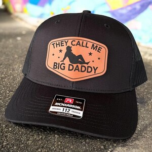 Op de afbeelding: Zwarte truckerpet met een mesh achterkant en een gebogen klep. De pet heeft een bruine patch met de tekst "THEY CALL ME BIG DADDY" en een silhouet. De pet is verstelbaar en heeft een Richardson 112 Trucker label.
