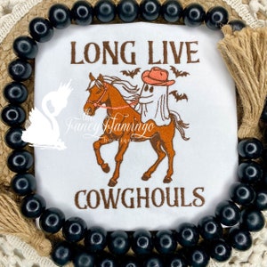 May include: White embroidered t-shirt with a ghost riding a brown horse. The ghost is wearing a red cowboy hat. The text "Long Live Cowghouls" is embroidered on the shirt.