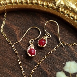 Op de afbeelding: Een paar gouden oorbellen met rode edelsteen druppels. De oorbellen hangen aan een gouden ketting.