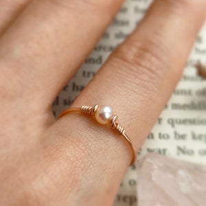 May include: A delicate gold ring with a single pearl accent. The ring is simple and elegant, perfect for everyday wear.
