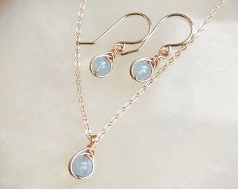 May include: A delicate gold necklace and matching earrings with light blue teardrop-shaped stones. The stones are set in gold wire.