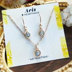 May include: A gold-filled jewelry set featuring a necklace and matching earrings. Each piece has a teardrop-shaped, wire-wrapped stone. The set is displayed on a card with the text "Aris HEARTMADE" and "14K Gold Filled."