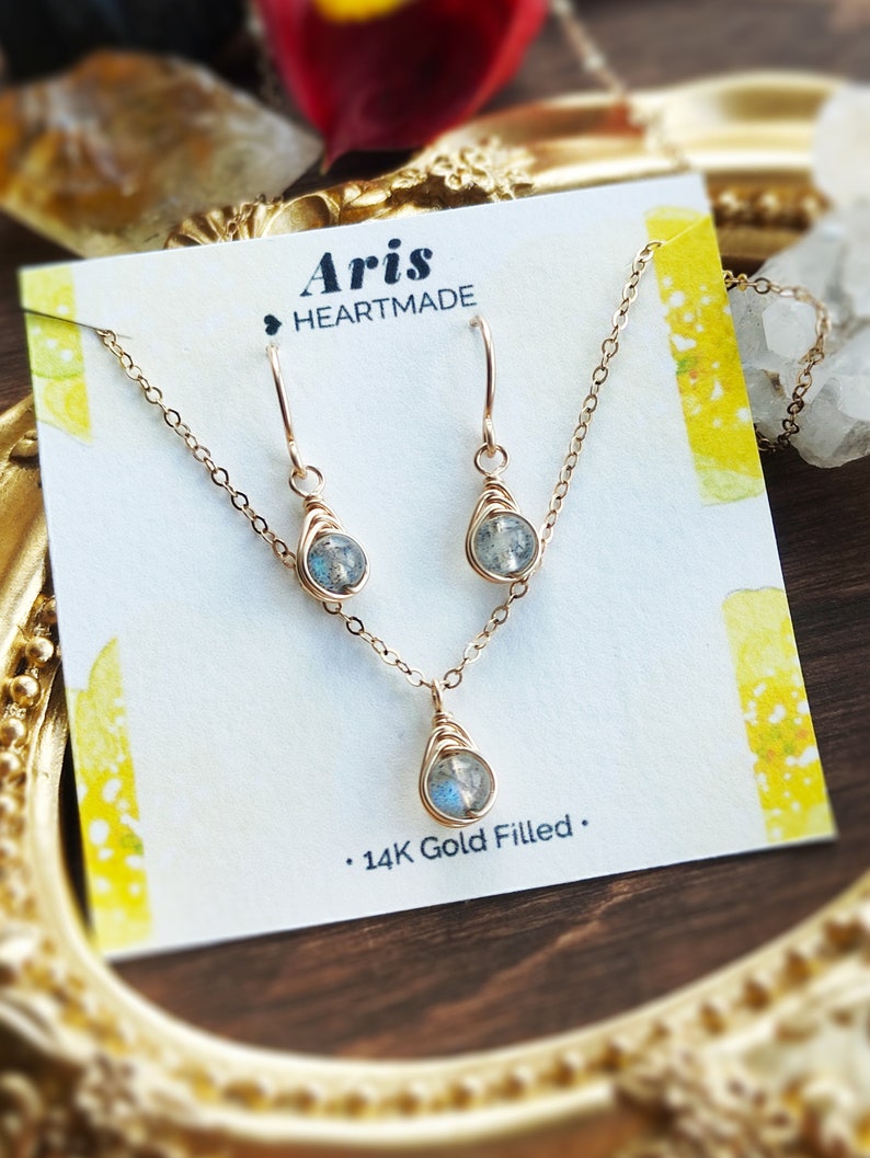 May include: A gold-filled jewelry set featuring a necklace and matching earrings. Each piece has a teardrop-shaped, wire-wrapped stone. The set is displayed on a card with the text "Aris HEARTMADE" and "14K Gold Filled."