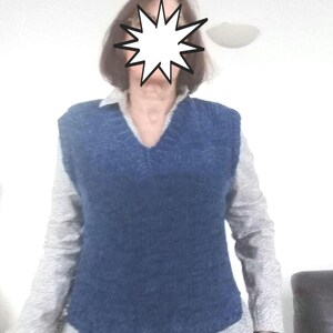 May include: A blue knitted vest with a v-neck. The vest is worn over a white long-sleeved shirt.