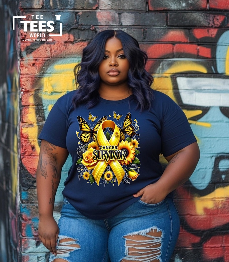 K&ouml;nnte beinhalten: Ein marineblaues T-Shirt mit einem gelben Band, Sonnenblumen und Schmetterlingen. Das Band tr&auml;gt den Schriftzug "Cancer Survivor".