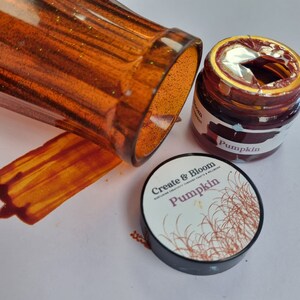 May include: Two jars of pumpkin-colored paint. One jar is open and the other is closed. The closed jar has a black label with the text "Create & Bloom" and "Pumpkin". The open jar has a red label with the text "Pumpkin".