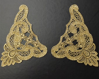 May include: Two gold-colored lace appliques with intricate floral designs. The appliques are triangular in shape and have a delicate, sparkly finish.