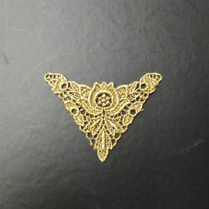 Peut inclure: Garniture en dentelle dorée de forme triangulaire avec un motif floral au centre.