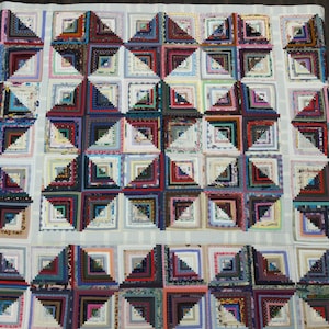 May include: A quilt made of colorful fabric squares, arranged in a pattern of log cabins. The quilt is made up of many different colors and patterns, including red, blue, green, and white.