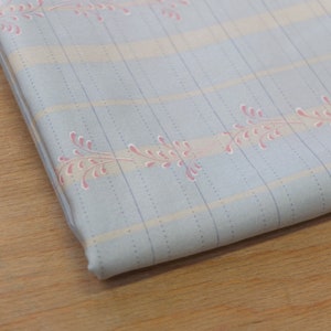 Könnte beinhalten: Ein hellblauer Stoff mit einem weißen und hellrosa floralen Muster. Der Stoff hat eine dezente gestreifte Textur.