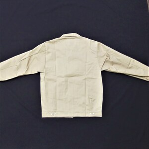 Puede incluir: Una chaqueta de trabajo beige con cierre de botones y mangas largas. La chaqueta tiene un dise&ntilde;o sencillo y est&aacute; hecha de un tejido resistente.