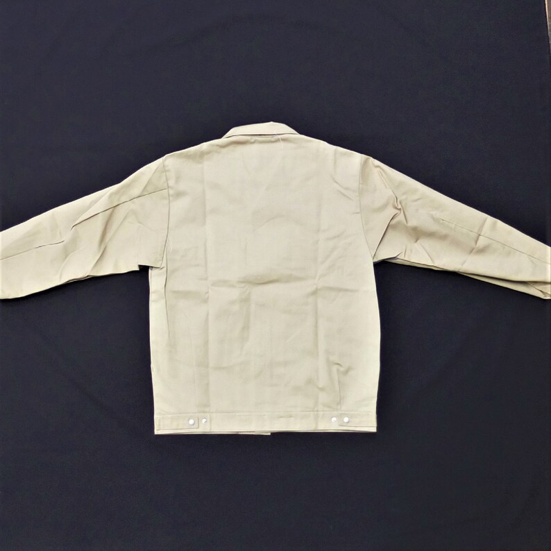 Puede incluir: Una chaqueta de trabajo beige con cierre de botones y mangas largas. La chaqueta tiene un dise&ntilde;o sencillo y est&aacute; hecha de un tejido resistente.