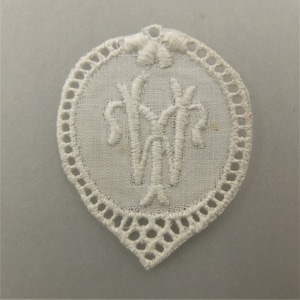 May include: White cotton lace applique with a scalloped edge and a monogram in the center.