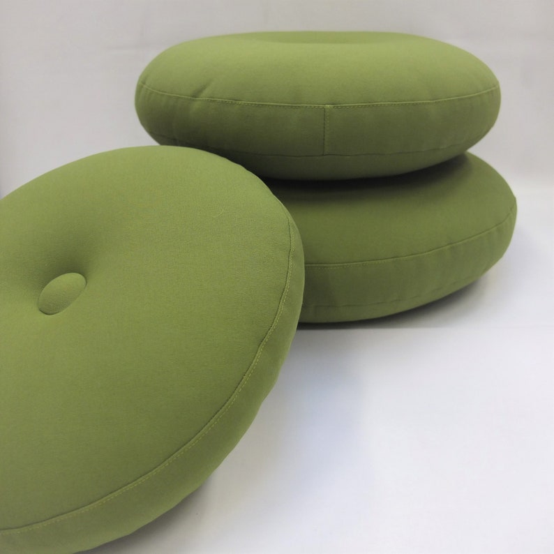May include: Three round green cushions stacked on top of each other. The top cushion has a button in the center.