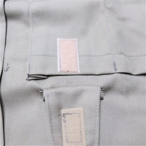 Puede incluir: Primer plano de una tela gris claro con dos parches rectangulares de tela beige. Los parches tienen una textura rugosa y est&aacute;n cosidos a la tela.