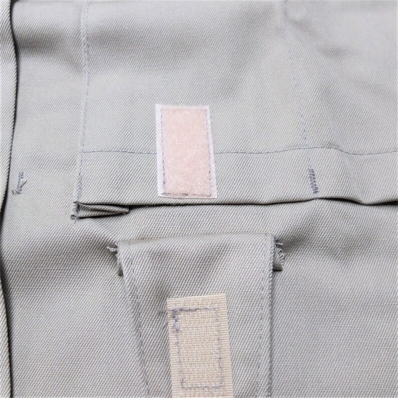 Puede incluir: Primer plano de una tela gris claro con dos parches rectangulares de tela beige. Los parches tienen una textura rugosa y est&aacute;n cosidos a la tela.