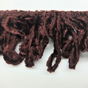 May include: A close-up of a brown velvet fringe trim. The fringe is made of soft, fluffy fibers and has a slightly textured appearance.
